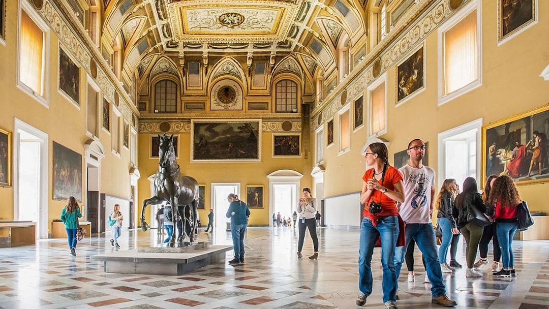 Visitors exploring the grand hall of the Archaeological Museum of Naples with statues and paintings.