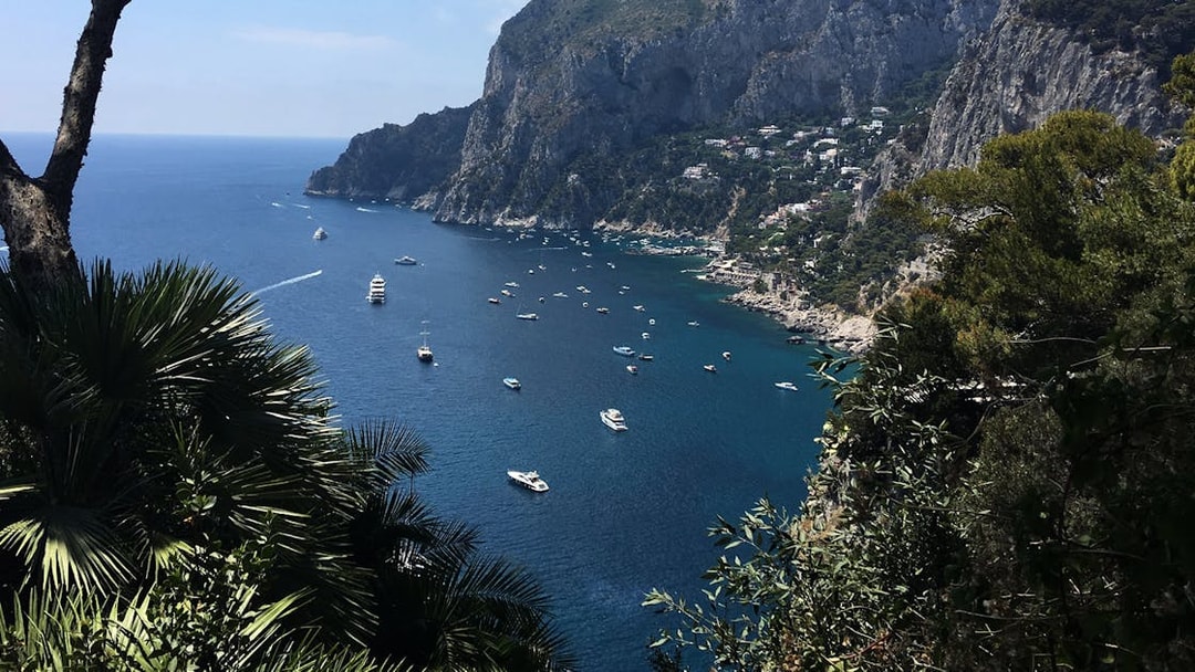 Boats on the blue waters of Capri Island with rocky cliffs and greenery, view from Naples day trip.