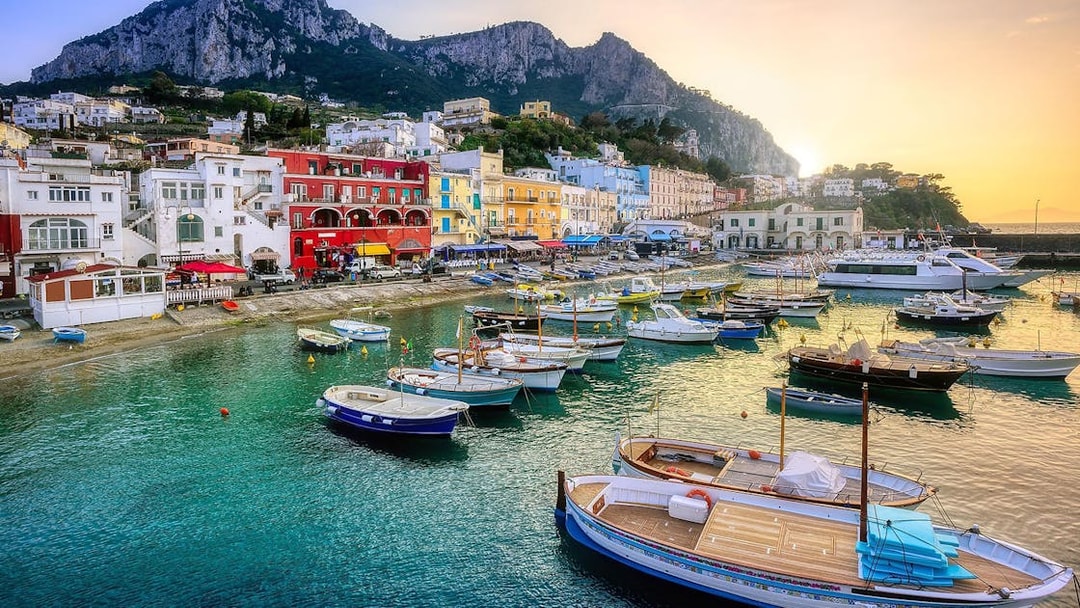 Boats in Marina Grande, Capri Island, with colorful buildings and cliffs in the background.