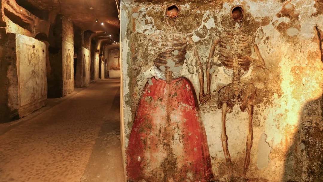 Skeletons in Catacombs of San Gaudioso, Naples, with painted clothing on walls.