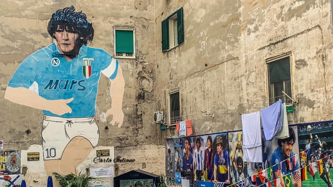 Mural of Diego Maradona in Naples, Italy, with surrounding tribute photos.