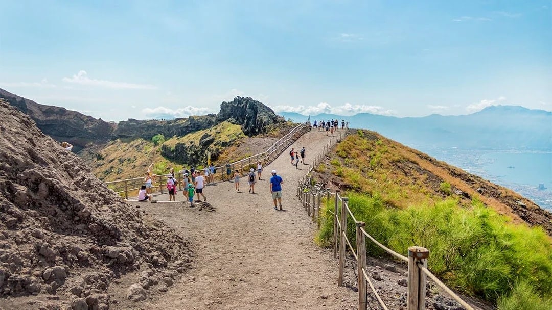 Hikers walking on a trail along Mount Vesuvius with a view of the surrounding landscape.