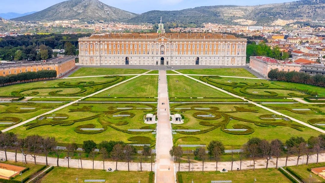 Royal Palace of Caserta with expansive gardens and mountain backdrop.