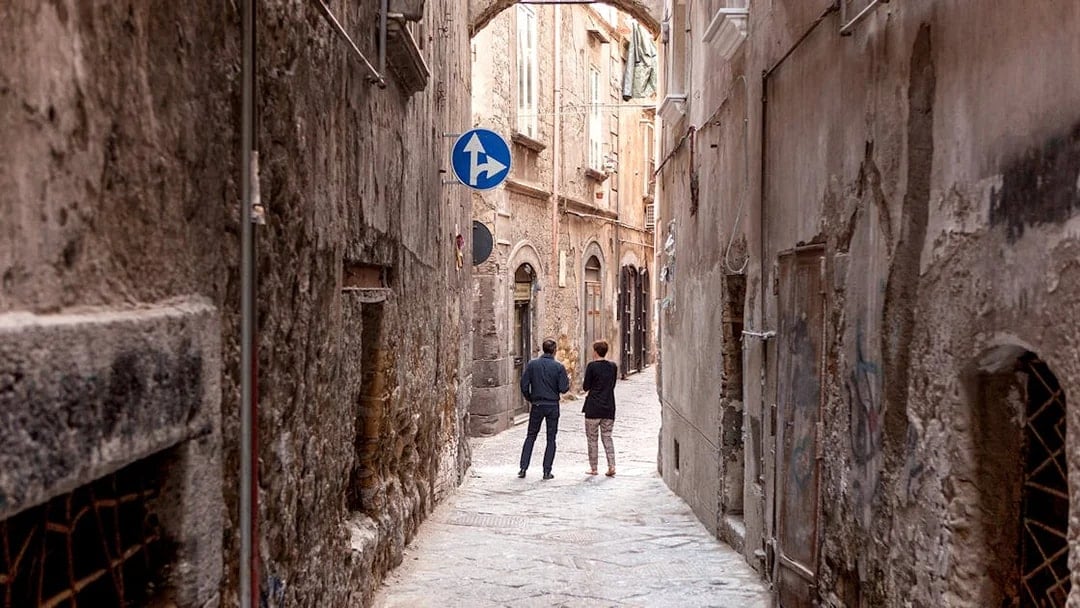 Narrow alleyway in Naples with two people walking under an archway.
