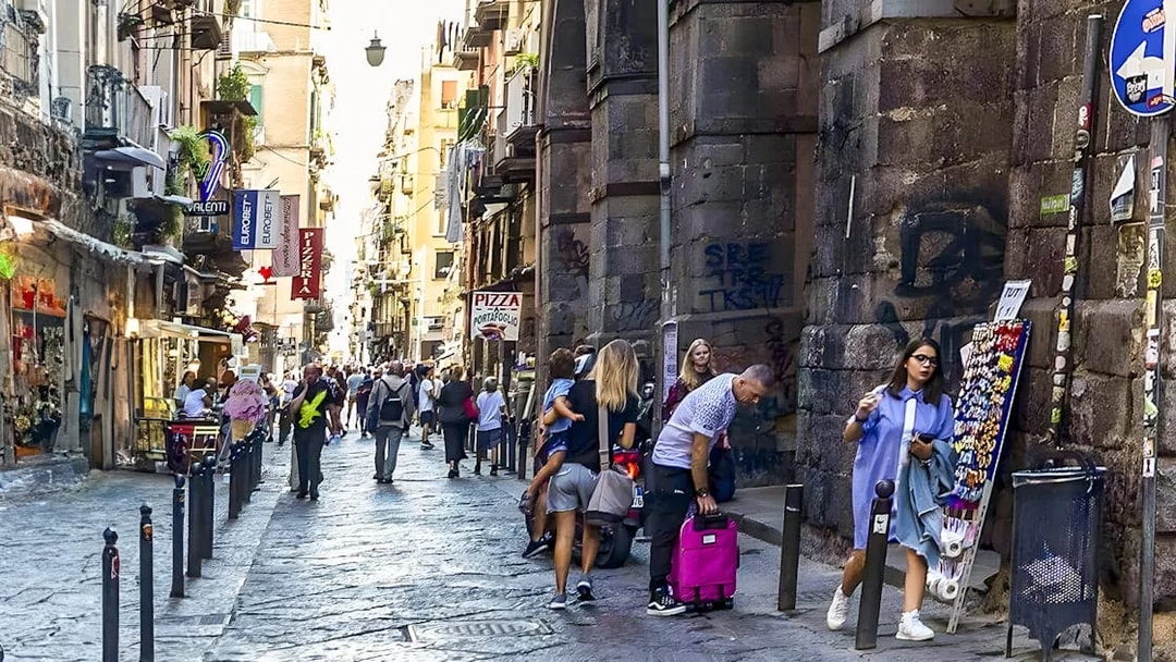Exploring bustling historic alley in Naples with shops and tourists.
