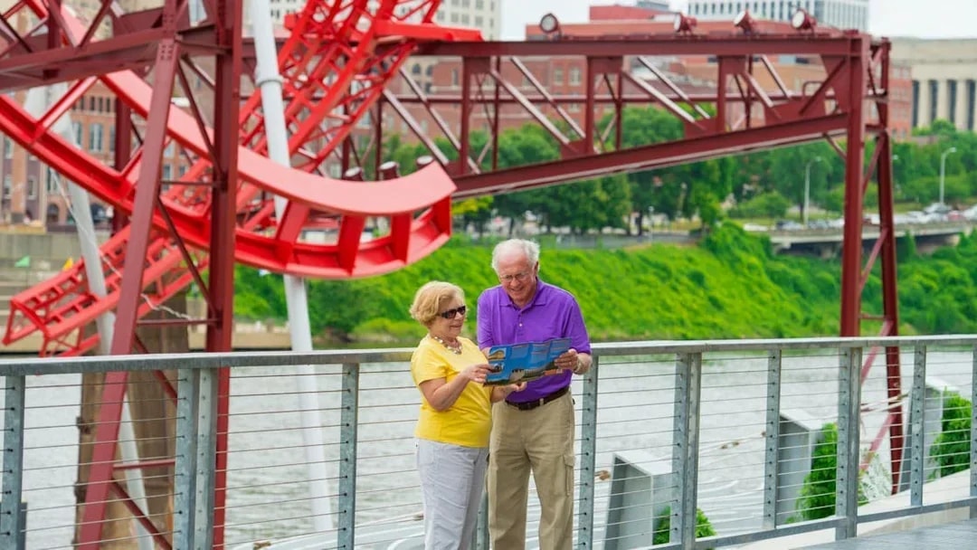 Elderly couple reading a map near a red sculpture on a Nashville riverfront walkway.