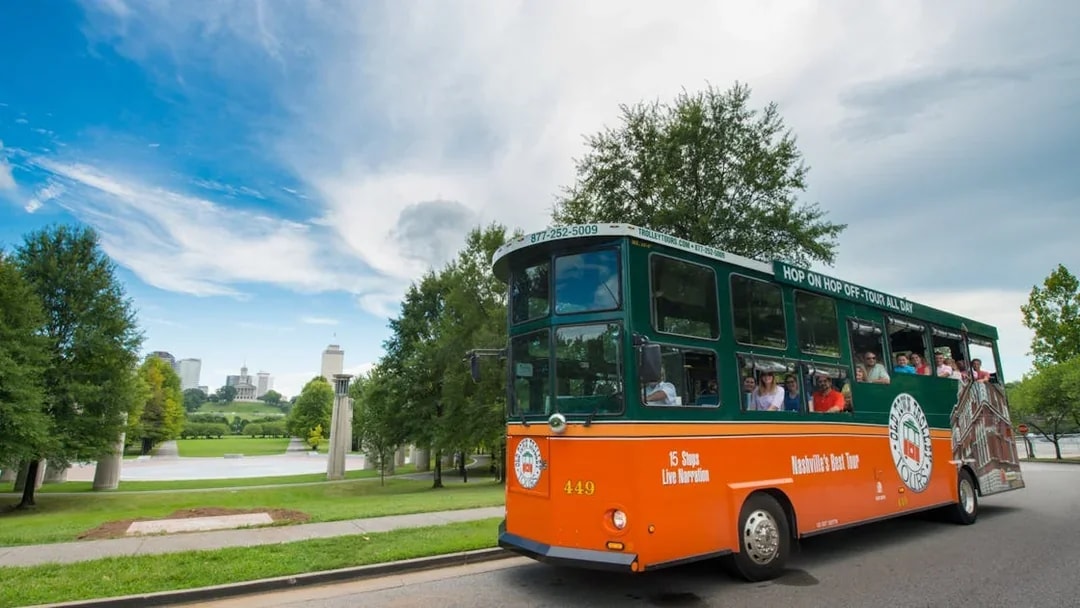 Nashville hop-on hop-off trolley with tourists, city skyline in background.