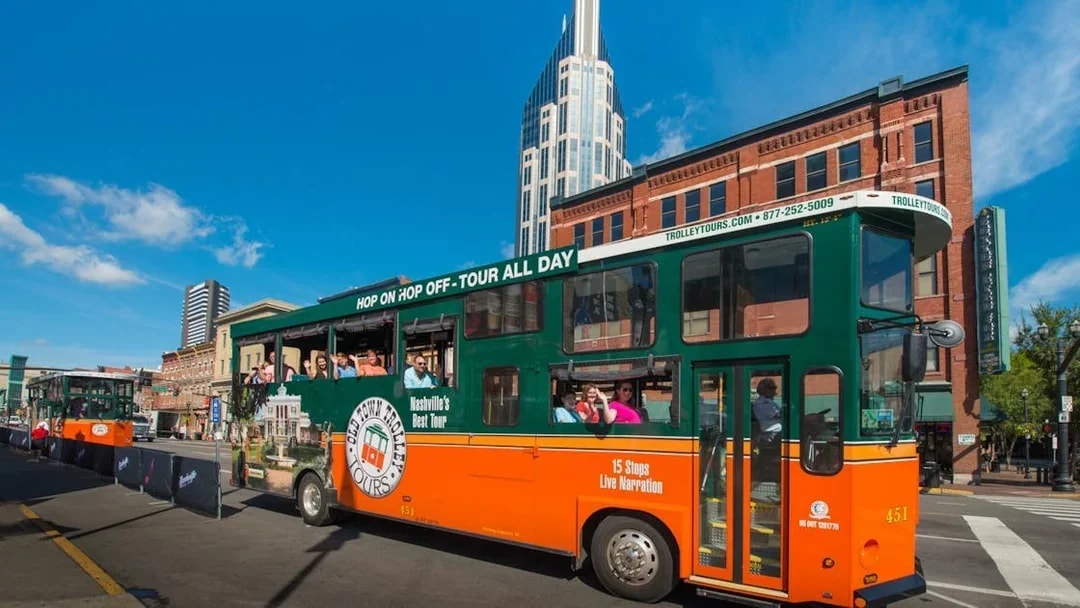 Nashville Old Town Trolley with tourists on a city street, featuring a tall building in the background.