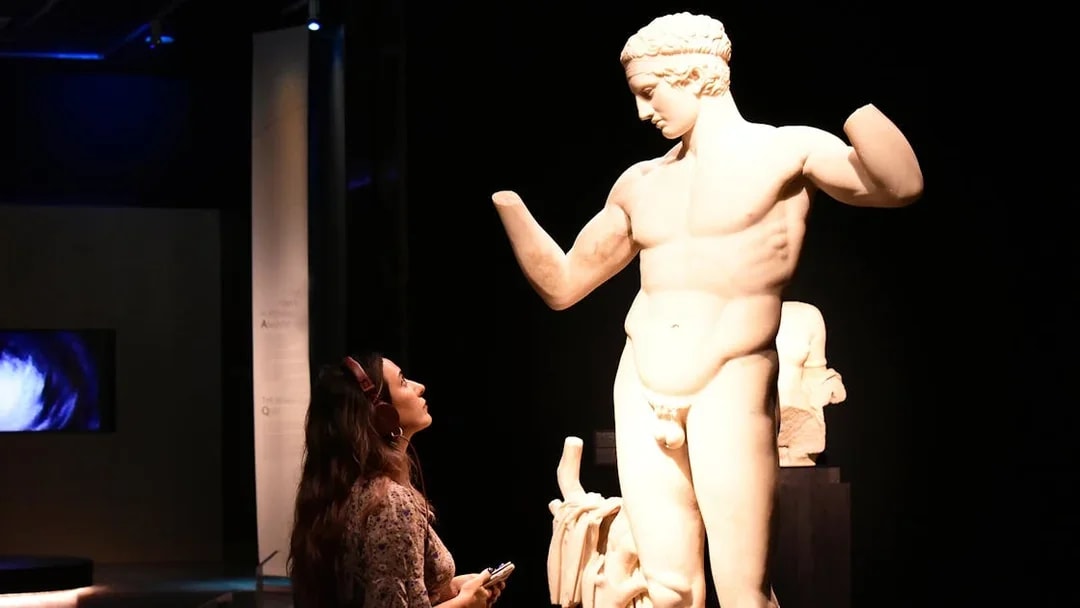 Visitor with audio guide admiring a classical statue at the National Archaeological Museum.