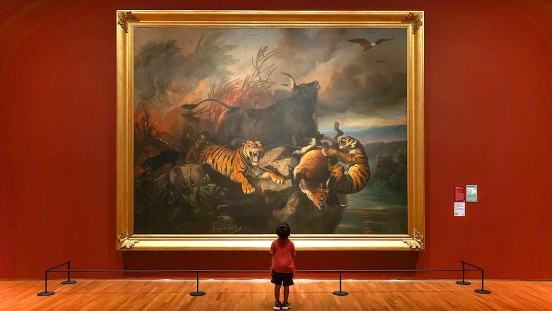Child viewing a large painting of tigers and wildlife at National Gallery Singapore.