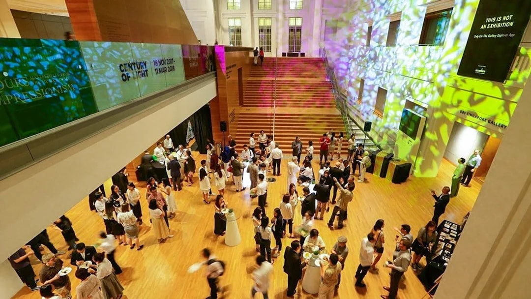 Visitors at National Gallery Singapore event in a brightly lit hall with colorful projections.