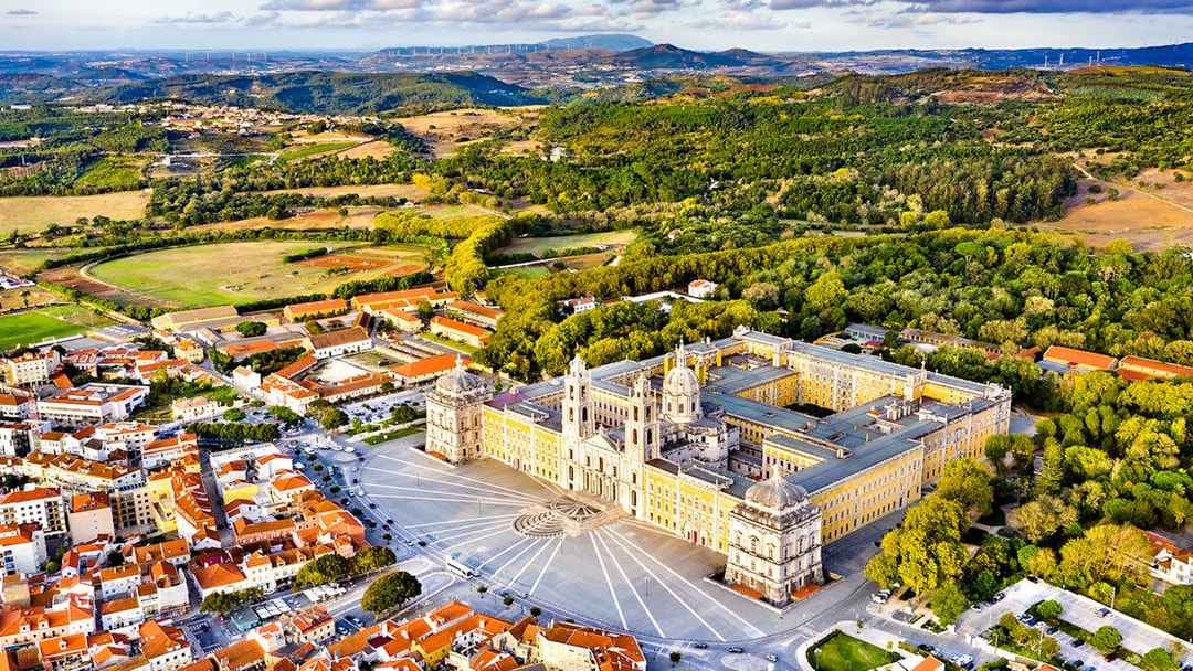 Aerial view of the National Palace of Mafra, Portugal, surrounded by lush greenery and town buildings.