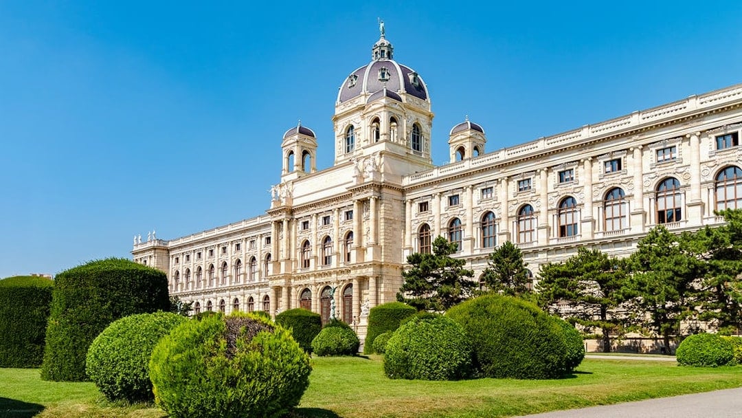 Natural History Museum in Vienna with manicured gardens and blue sky.