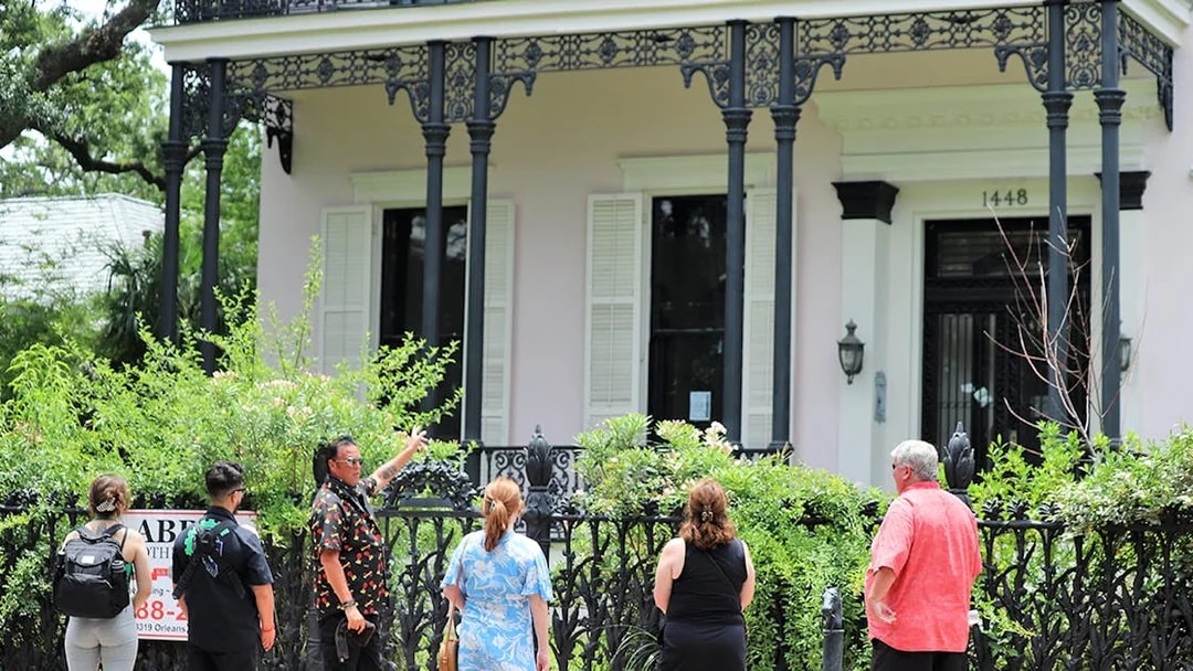Tour group exploring historic house in New Orleans with ornate ironwork balcony.