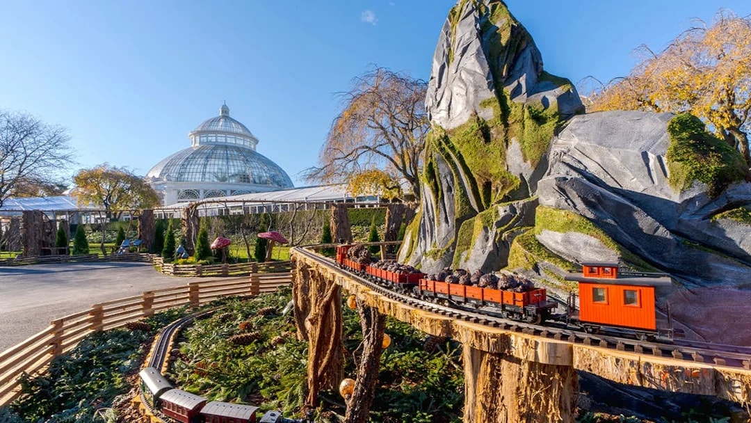 Holiday Train Show model train at New York Botanical Gardens with conservatory in background.