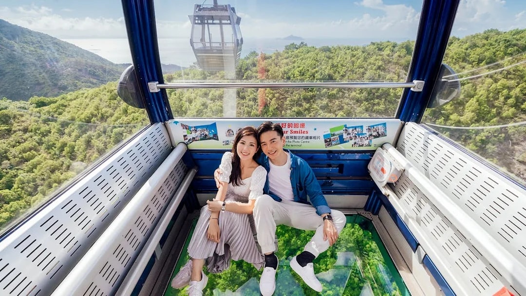 Couple enjoying a ride in a crystal cabin cable car with scenic views of lush greenery below.