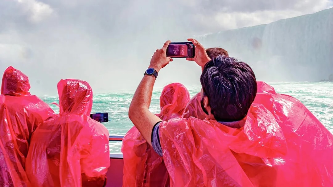 Passengers in red ponchos on Hornblower Cruise at Niagara Falls, Canada, taking photos.