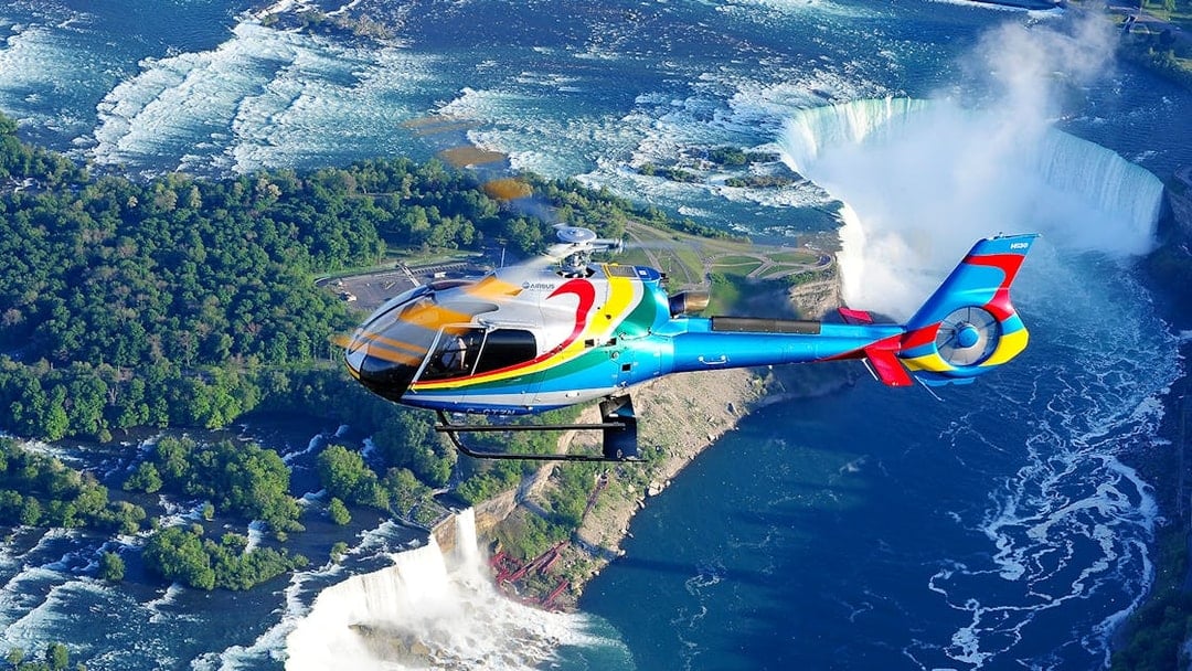 Helicopter flying over Niagara Falls with a view of the waterfalls and surrounding landscape.