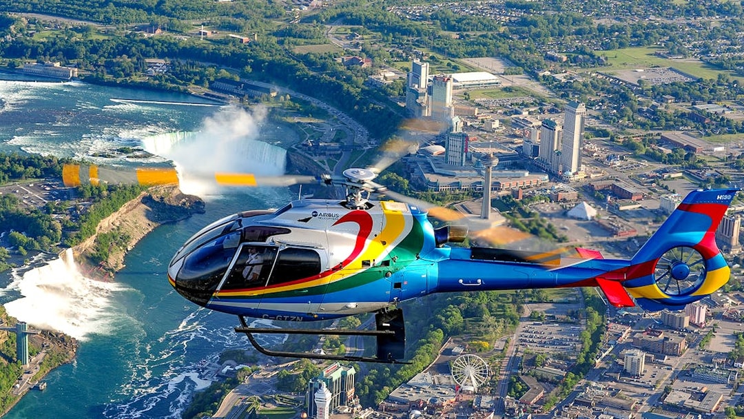 Helicopter flying over Niagara Falls with cityscape in the background.