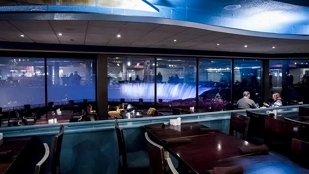 Dining area with view of illuminated Horseshoe Falls through large windows.