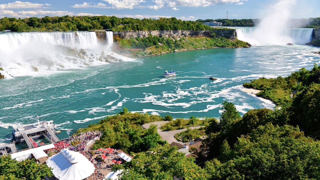 Niagara Falls with American and Bridal Veil Falls, boat on river, lush greenery.