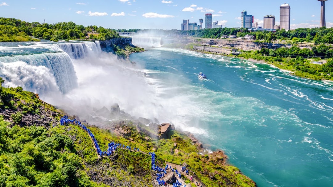 Aerial view of Niagara Falls with tourists in blue ponchos and a boat on the river.