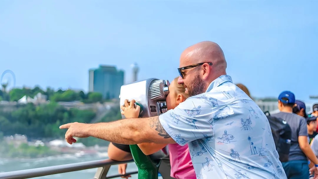 Man and child using binoculars at observation point overlooking cityscape.