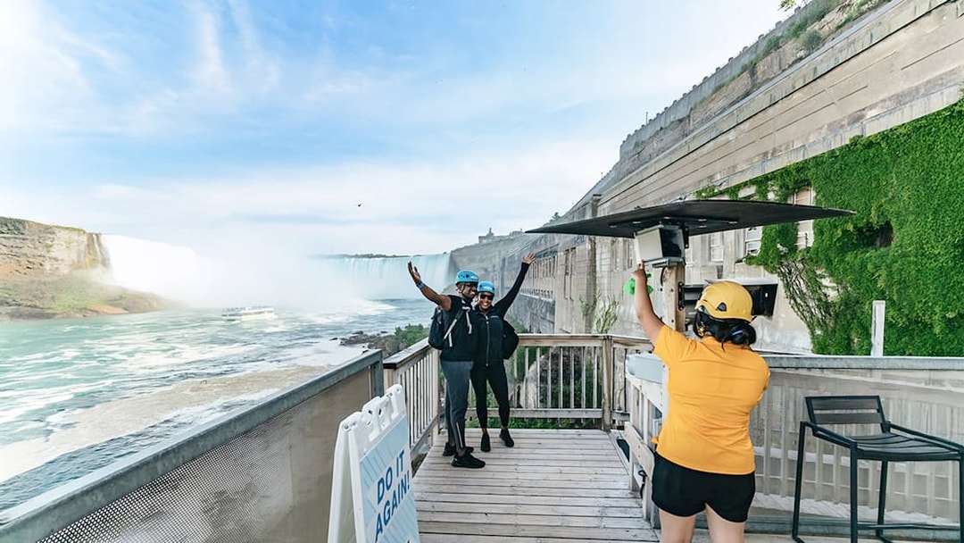 Visitors preparing for a zipline ride with a view of Niagara Falls in the background.