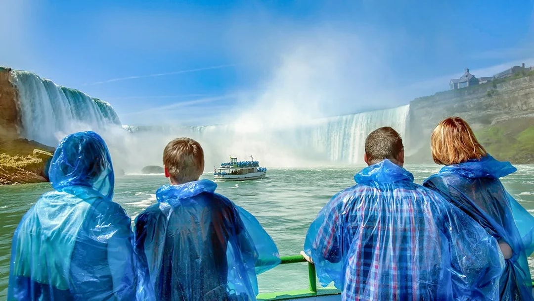 Tourists in blue ponchos on a Niagara Falls cruise boat approaching the waterfall.