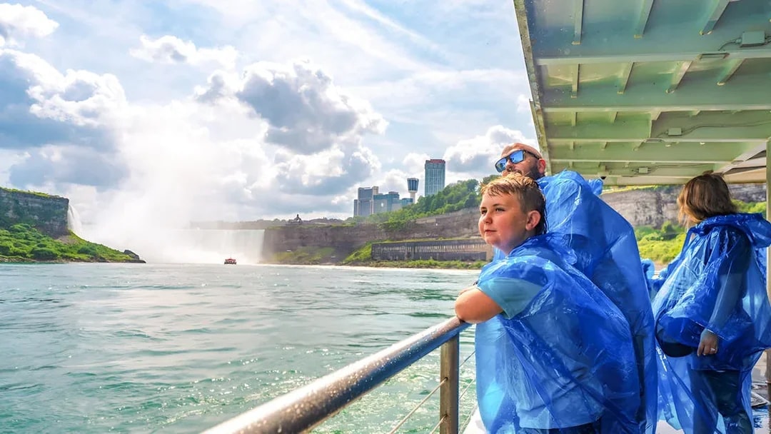 Family on a boat tour at Niagara Falls, wearing blue ponchos, with mist and skyline in view.