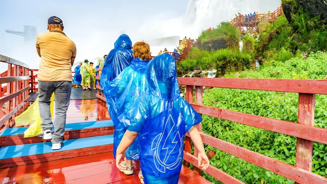 Visitors in blue ponchos walking on a wooden walkway near Niagara Falls.
