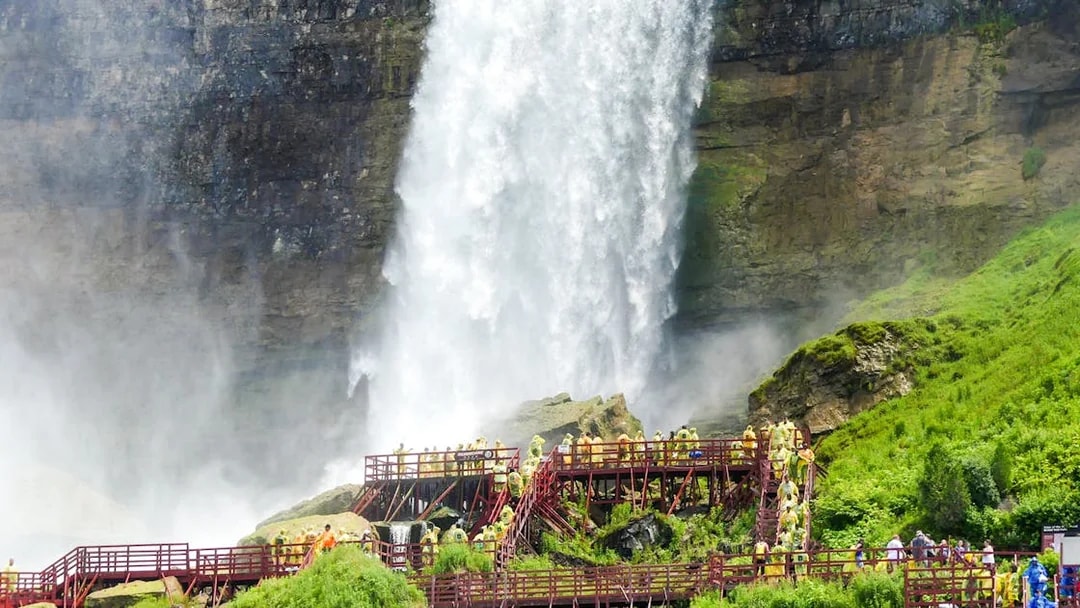 Visitors on wooden walkways near Bridal Veil Falls, Niagara, with mist and lush greenery.