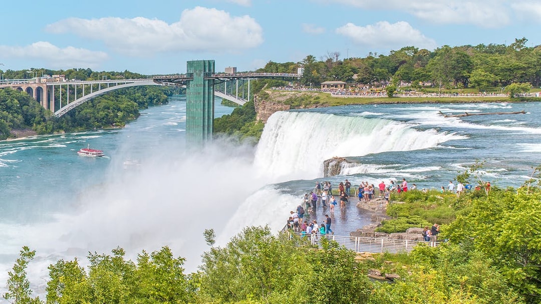 Visitors on Luna Island viewing Niagara Falls with Rainbow Bridge in the background.