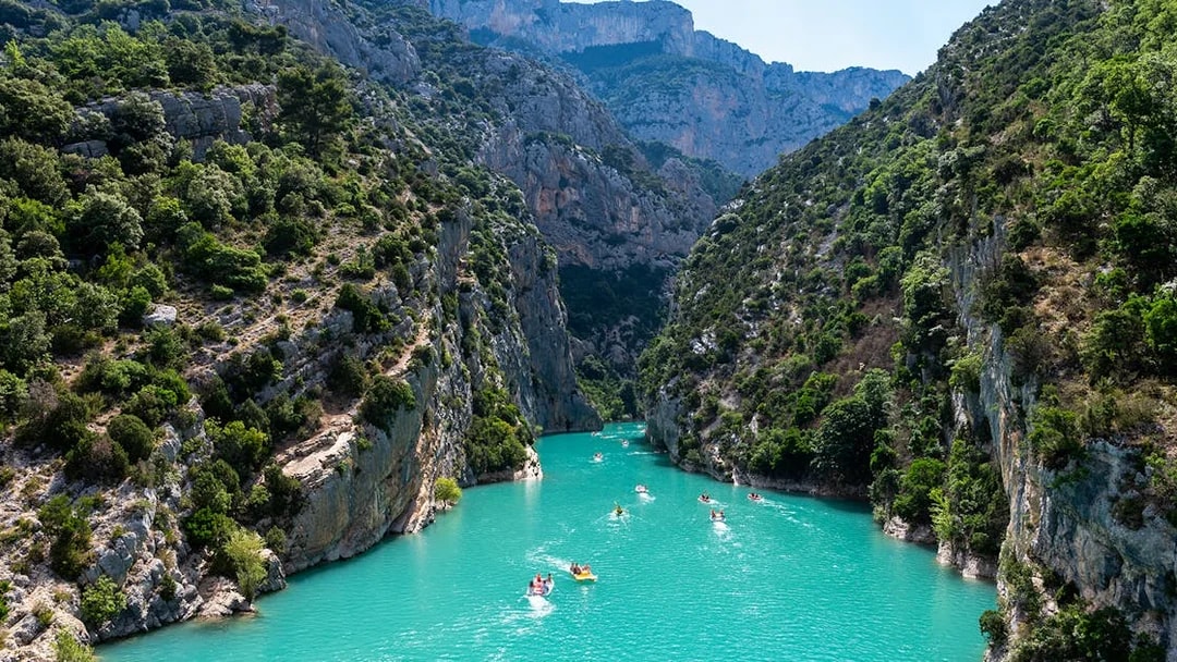 Kayakers on turquoise waters of Gorges du Verdon, surrounded by steep cliffs and lush greenery.