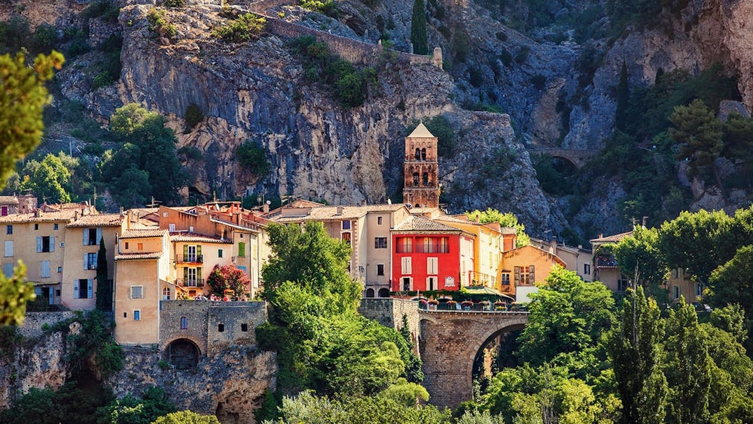 Moustiers Sainte Marie village with colorful buildings and church tower against rocky cliffs.
