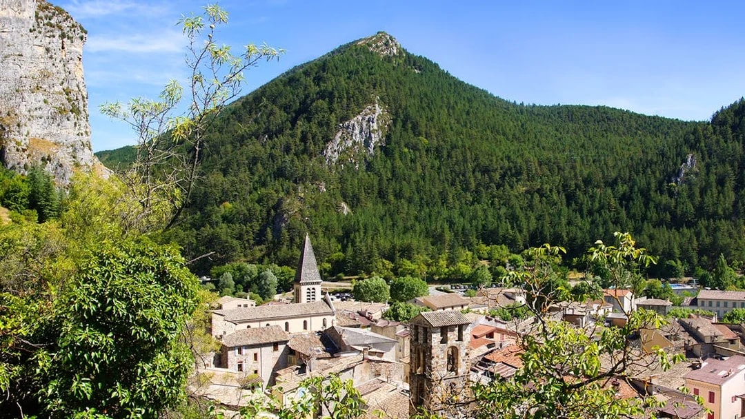Village nestled in the Gorges du Verdon with a church spire and forested mountains.
