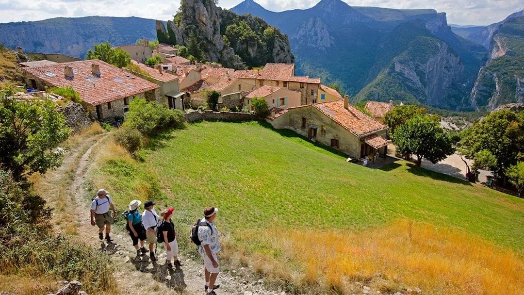 Hikers walking through a village with Gorges du Verdon cliffs in the background.