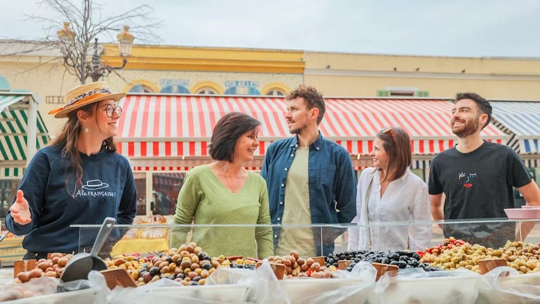 Tour group exploring a market in Nice with a guide, featuring colorful stalls and local produce.