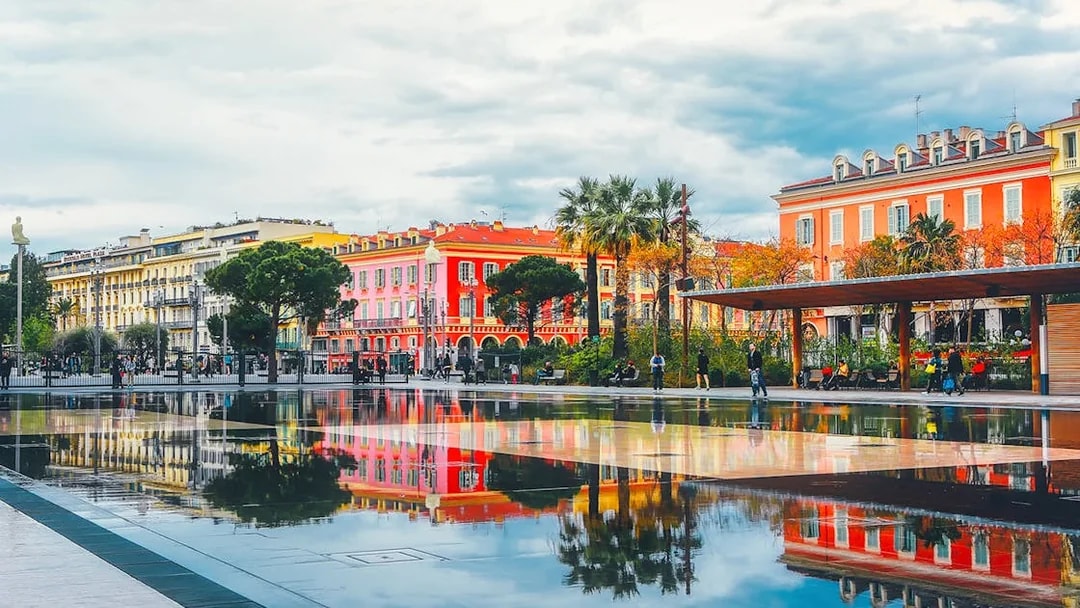 Colorful buildings and palm trees reflected in a water mirror in Nice, France.