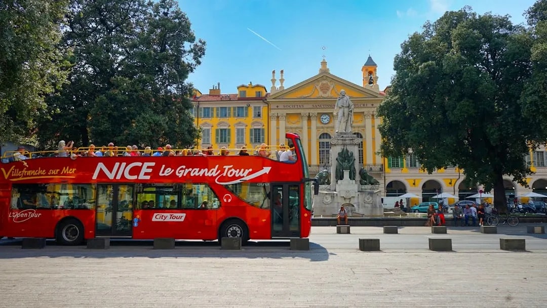 Hop-on hop-off bus in Nice, France, near a historic building and statue.