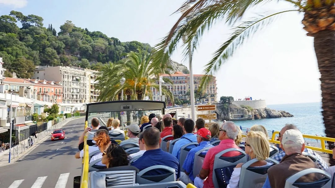Open-top bus tour along Nice coastline with palm trees and sea view.
