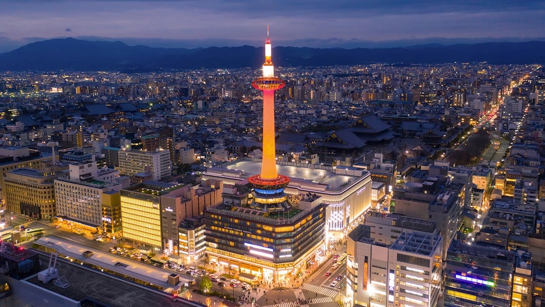 Kyoto Tower illuminated at night with cityscape in the background.