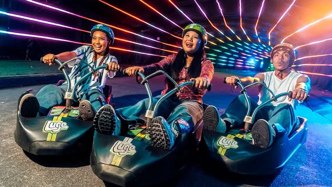 Friends enjoying night luge ride under colorful lights in Singapore.
