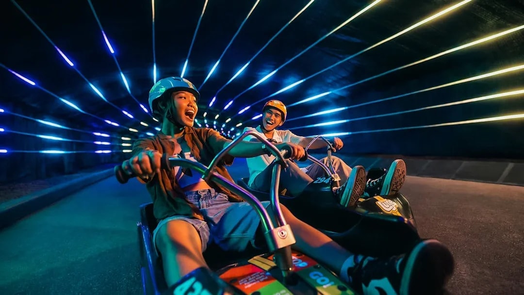 Friends enjoying night luge ride in illuminated tunnel, Singapore.