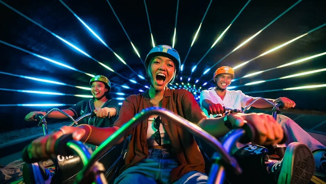 Friends enjoying night luge ride in illuminated tunnel, Singapore.