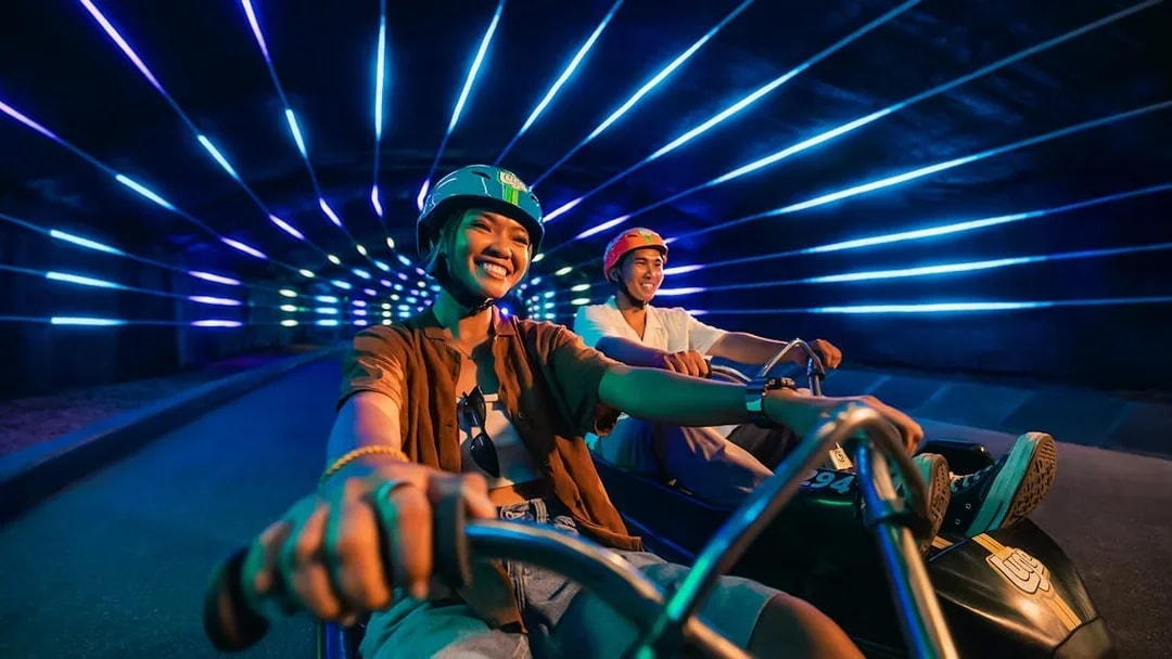 Friends enjoying night luge ride in illuminated tunnel, Singapore.