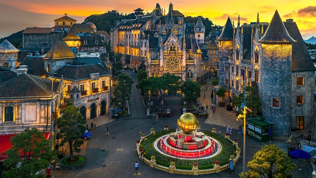 Central square of medieval city in Ba Na Hills Park, Da Nang, with illuminated buildings at sunset.