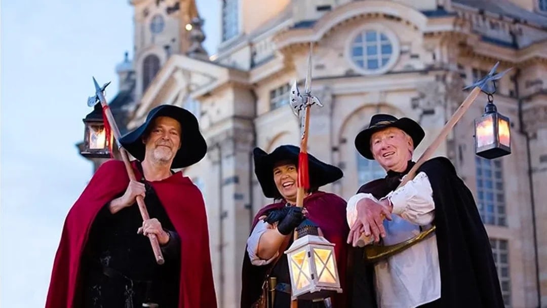 Night watchmen in traditional attire with lanterns in front of Dresden's Frauenkirche.