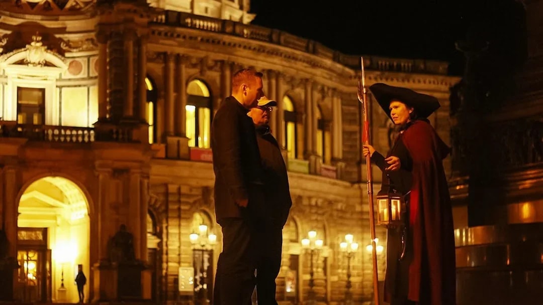 Night watchman guiding a tour in front of illuminated Dresden architecture.