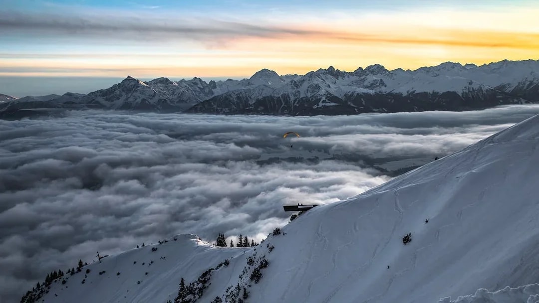 Paraglider over snowy Alps at sunset, Top of Innsbruck PLUS.
